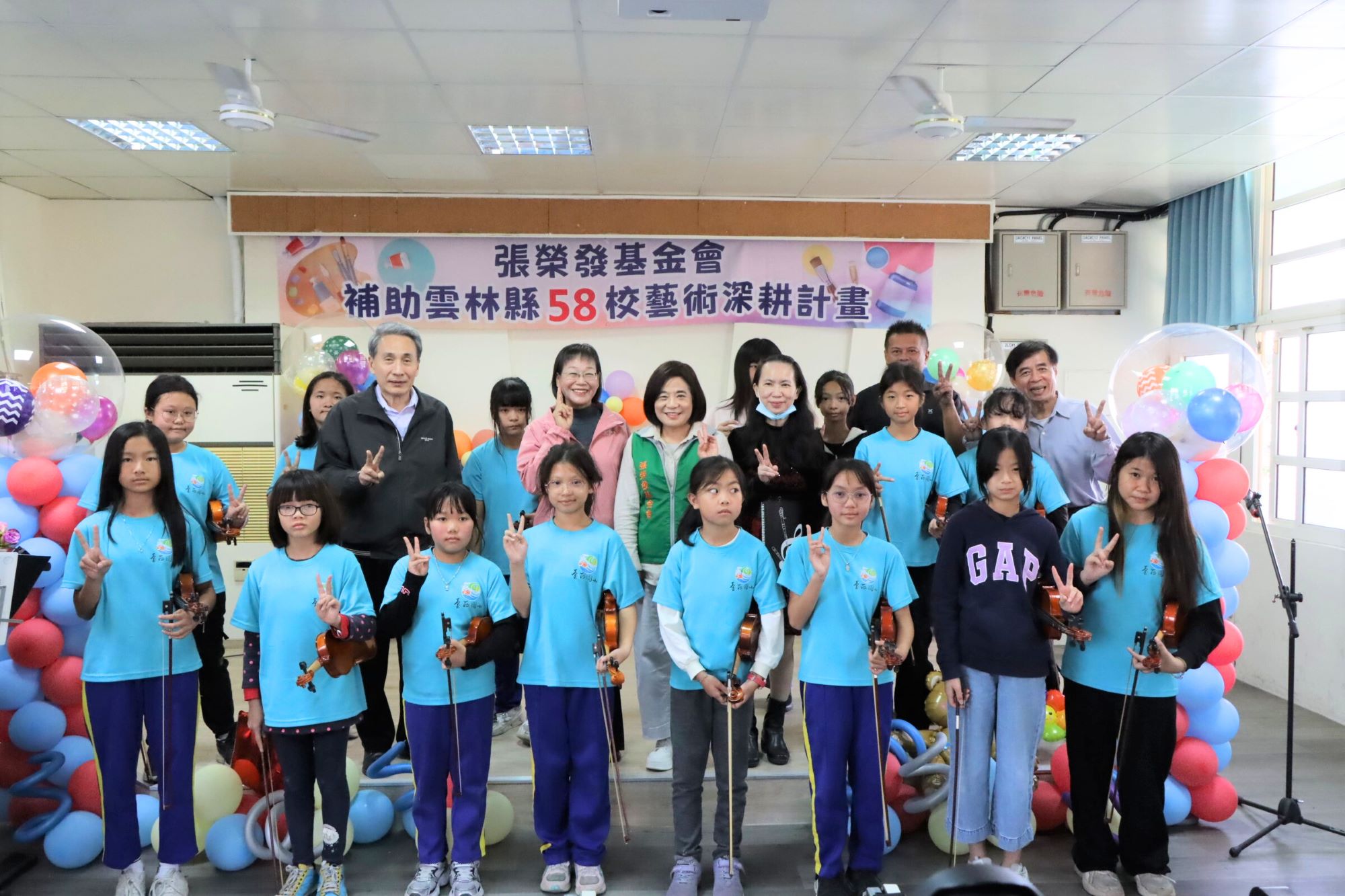臺西國小小朋友展現小提琴學習成果，執行長鍾德美（中著綠背心）、雲林縣副縣長謝淑亞（第二排左三）、雲林縣政府教育處處長邱孝文（第二排左二）、臺西國小校長蔡維哲（第三排右一）與學童一同合影。