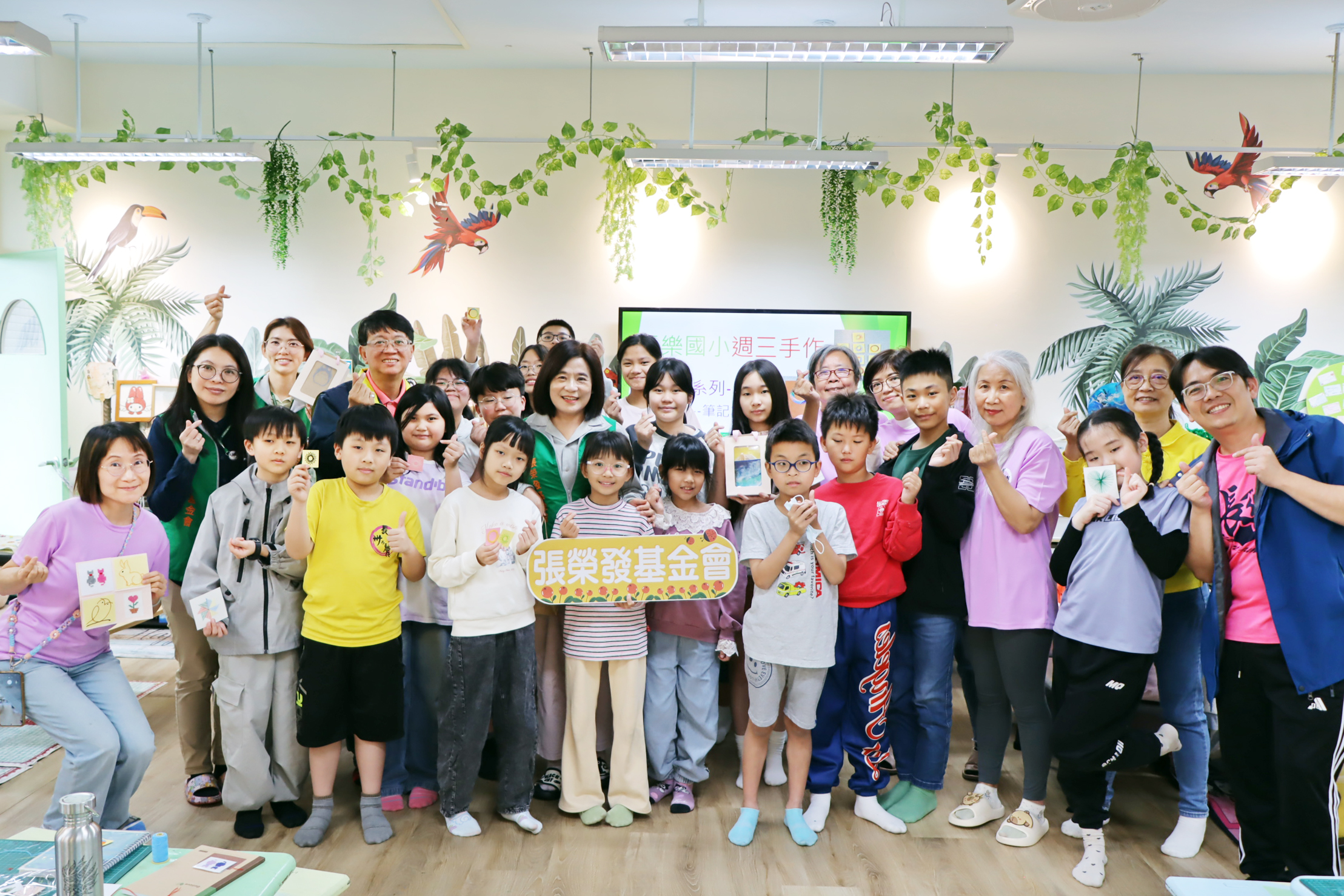 張榮發基金會執行長鍾德美(中著綠背心)與基隆市長樂國小創課社團師生持刺繡作品合影。